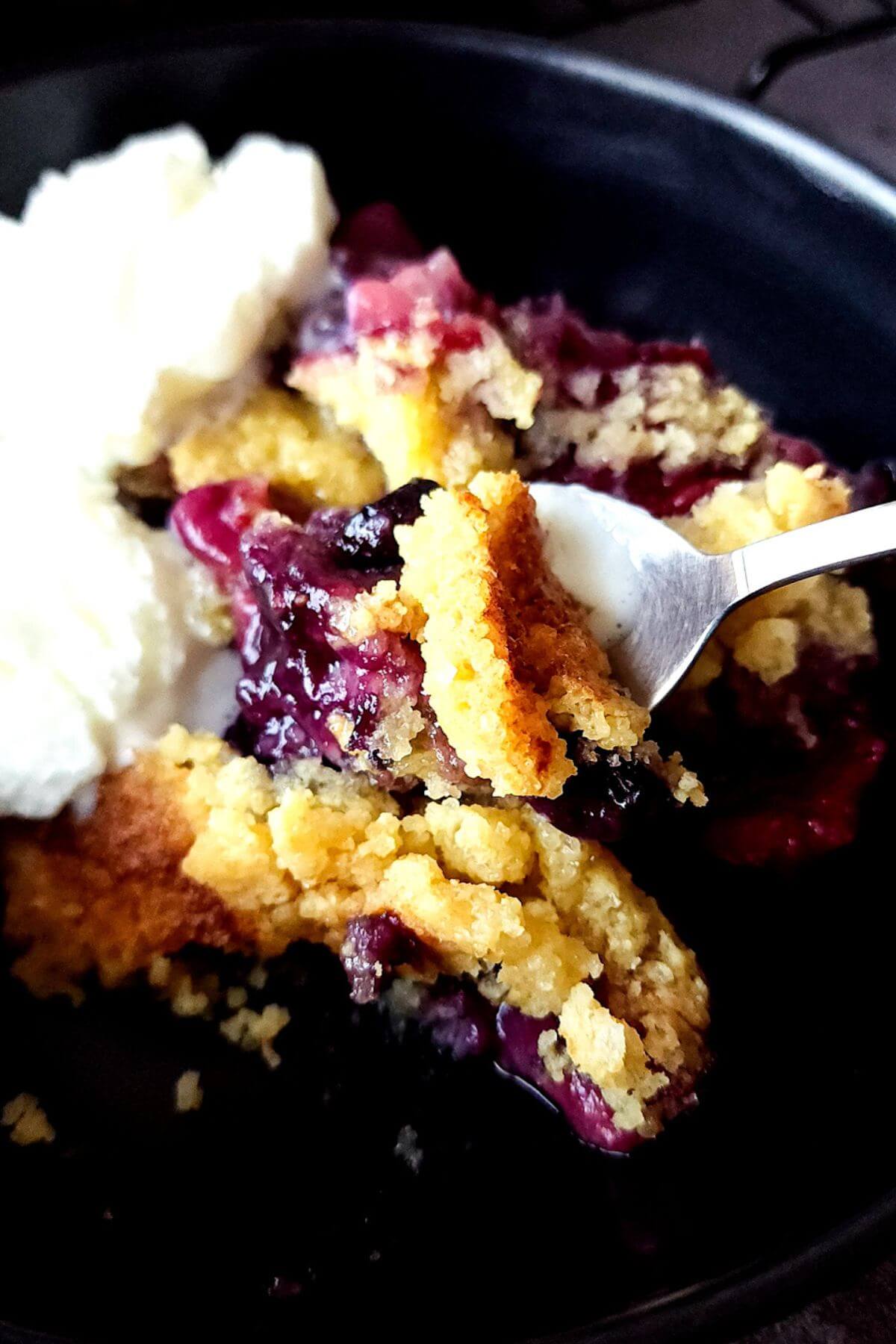 A spoonful of cobbler lifted over a bowl of mixed berries cobbler and vanilla ice cream.