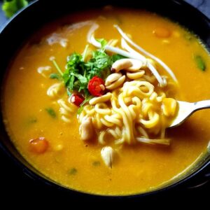 A bowl of Thai pumpkin ramen soup with a fork.