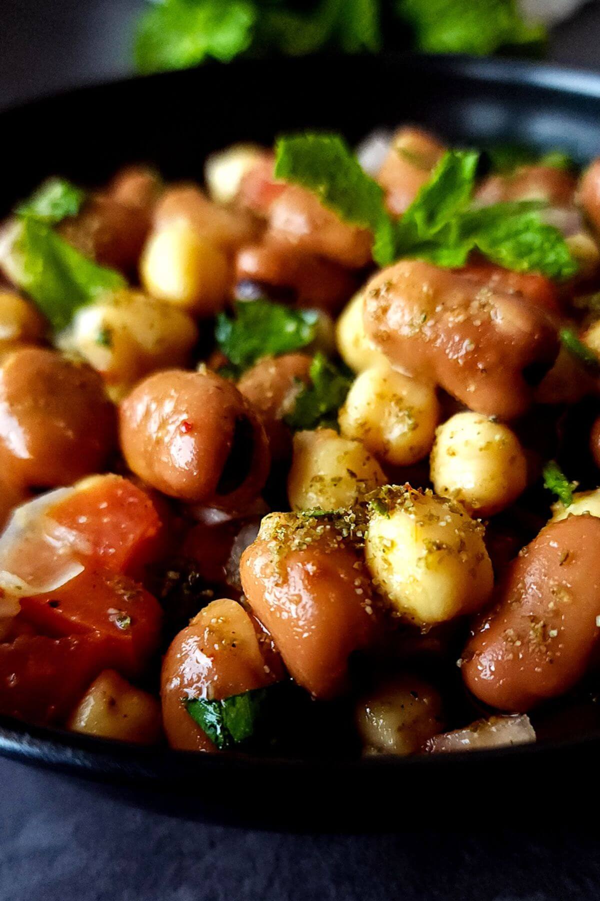 A bowl of fava bean and chickpea salad garnished with fresh herbs.