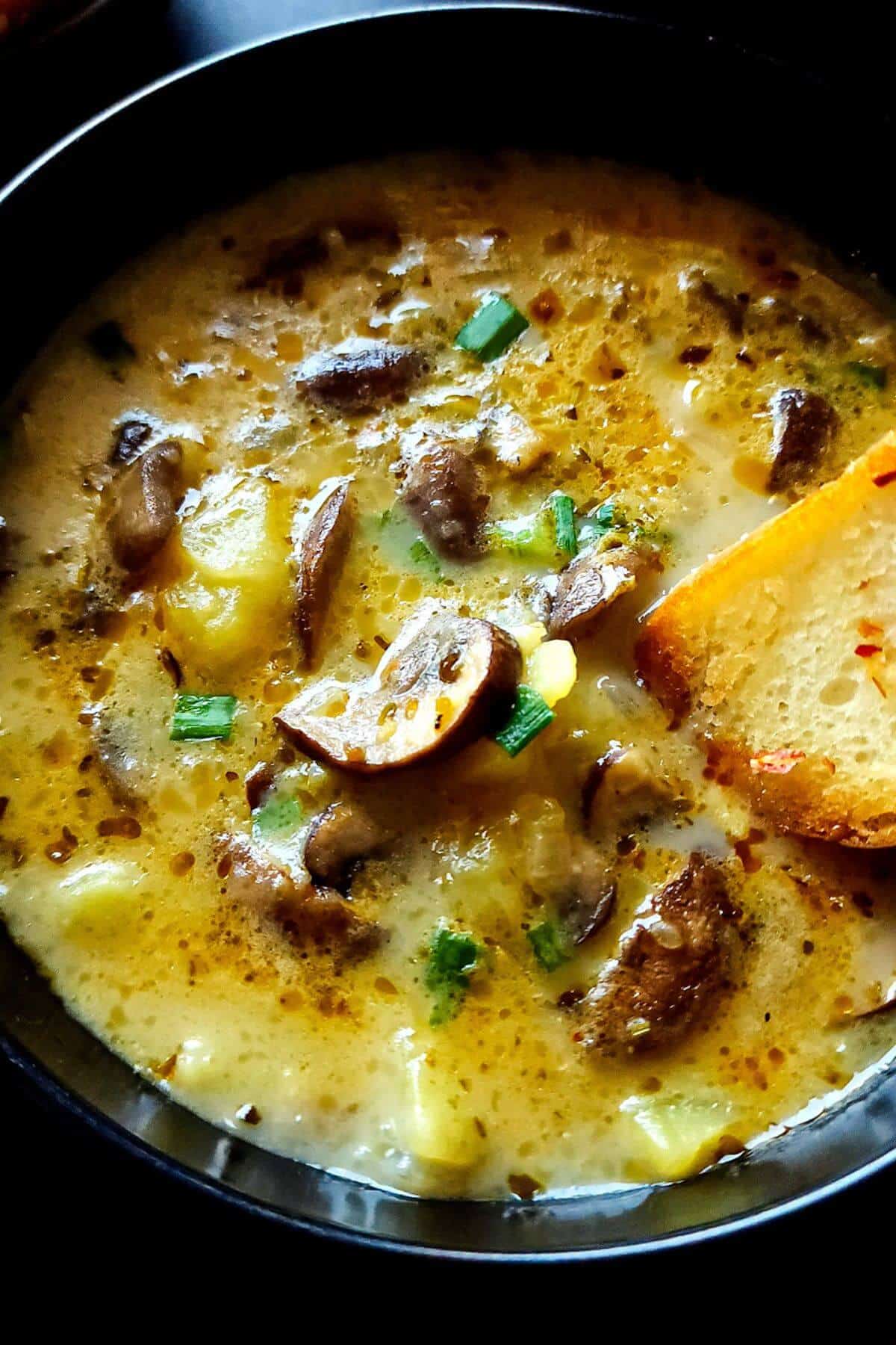 Toasted bread dipped in a bowl of mushroom potato soup.