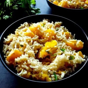 Pumpkin rice in a black bowl with fresh cilantro in the background.