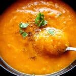 Roasted butternut squash and red pepper soup in a bowl with a spoon.