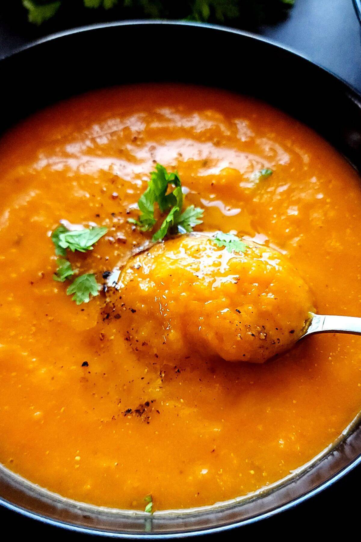Red pepper and butternut squash soup in a bowl with a spoon.