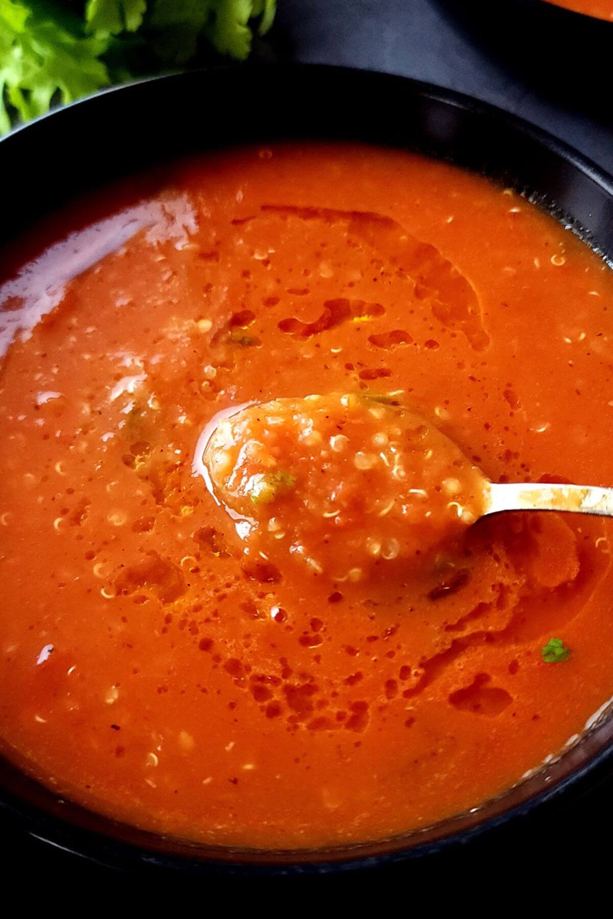 A bowl of tomato quinoa soup with a spoon.