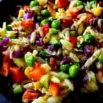 Rainbow orzo salad sprinkled with crushed black pepper.