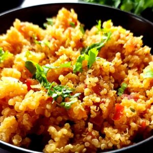A bowl of tomato quinoa garnished with chopped cilantro and crushed black pepper.