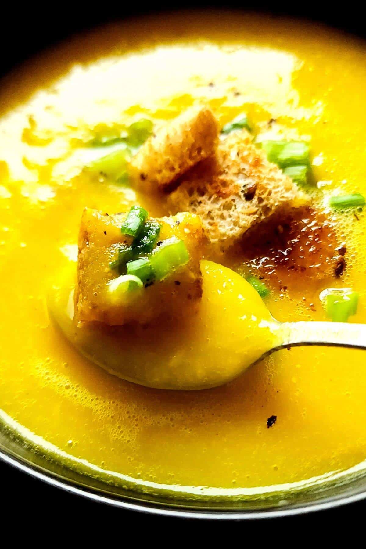 Yellow pepper and potato soup in a bowl with croutons and chopped spring onion.