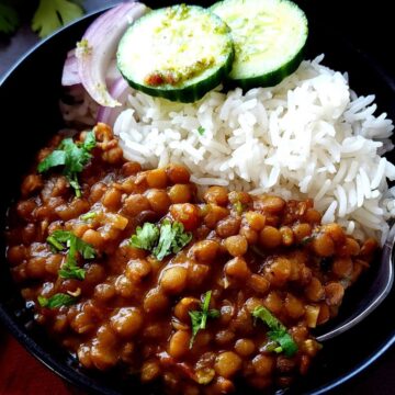 Green lentil curry and rice in a bowl with onion and cucumber slices.