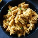 A bowl of creamy curry pasta garnished with chopped cilantro.