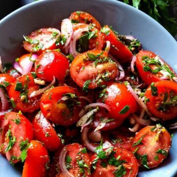 Lebanese tomato salad in a bowl with fresh parsley in the background.