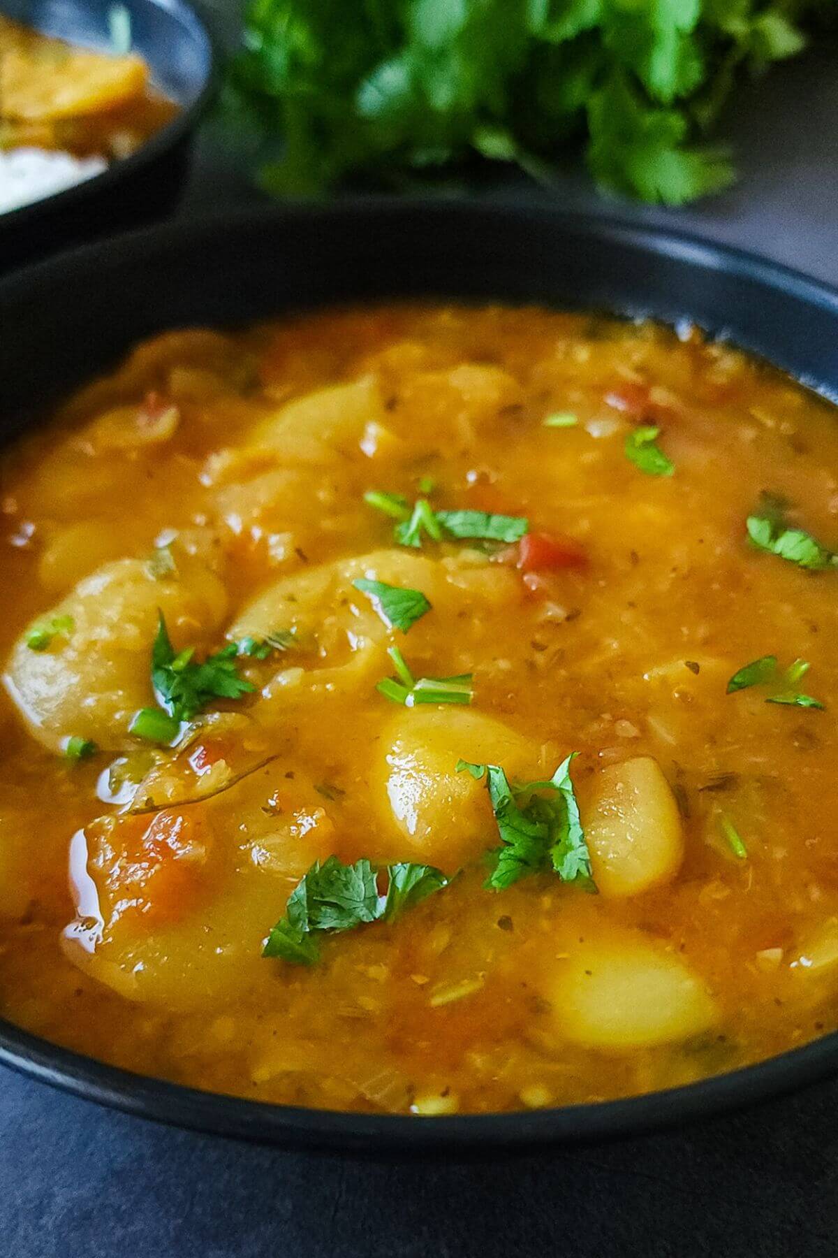 Curried butter beans garnished with chopped cilantro served in a black bowl.