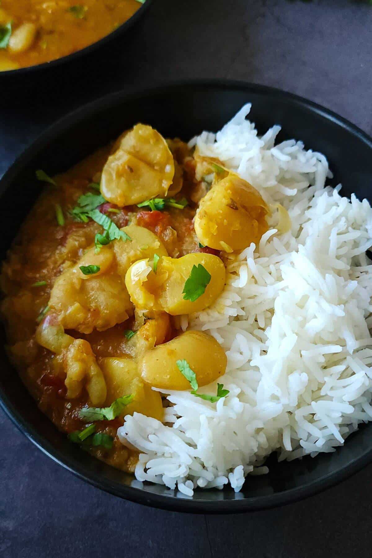 Curry butter beans and rice served in a black bowl.
