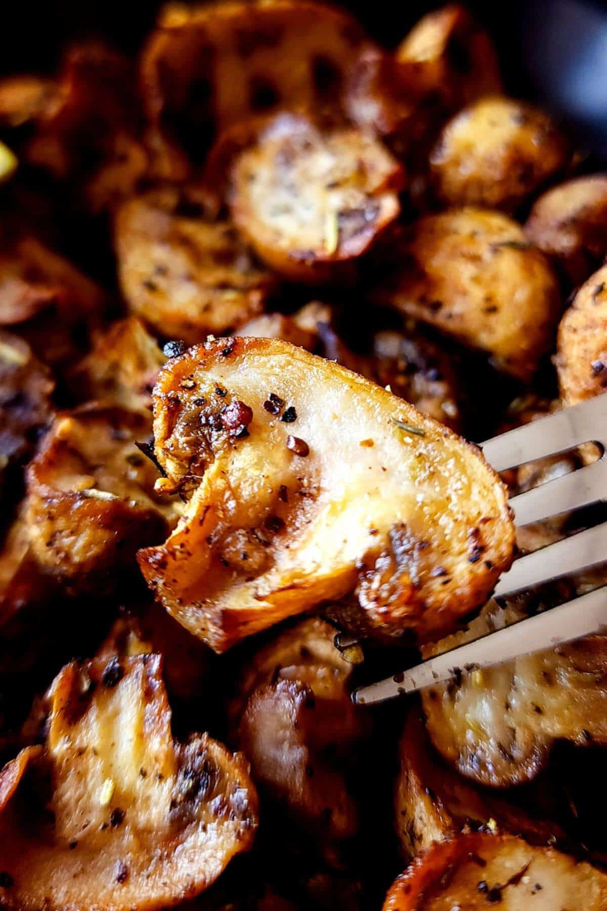 A slice of air fried mushroom on a fork lifted over a bowl of air fried mushrooms.